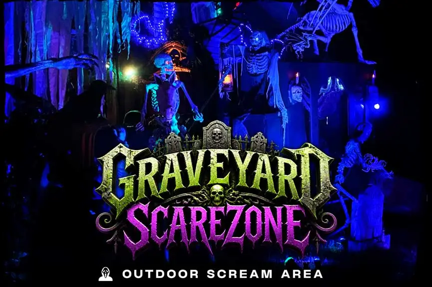 Eerie, blue-lit outdoor cemetery set design packed with hanging skeletons, creepy tombstones, and thick cobwebs to promote the Graveyard Scarezone attraction.